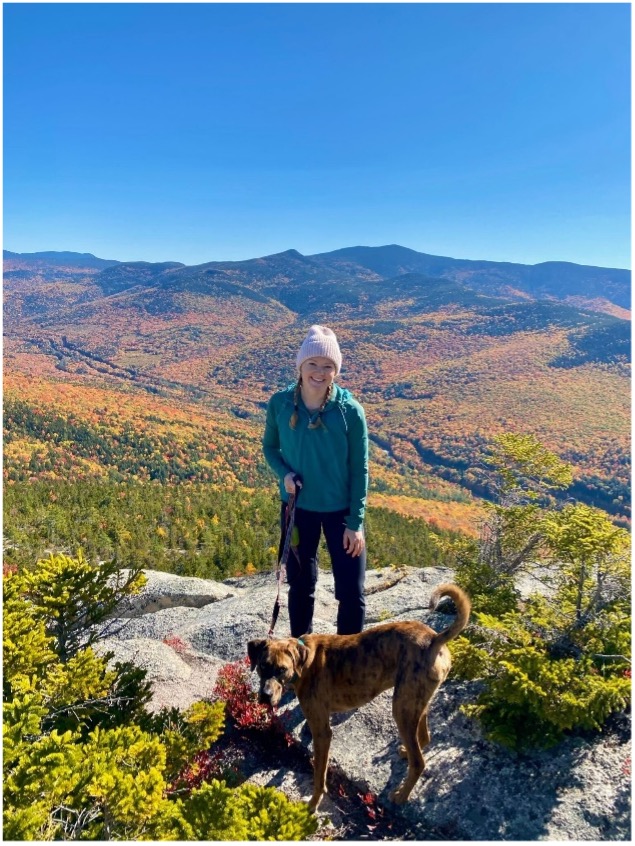 woman with dog wearing hat with mountain view behind her